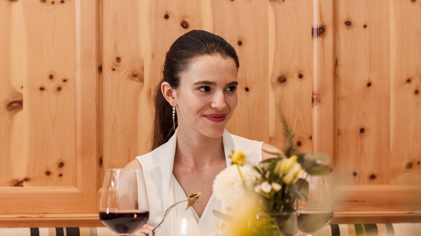 Brindiamo alle nostre mamme! Donna seduta a tavola apparecchiata con bicchiere di vino, candela e fiori al ristorante