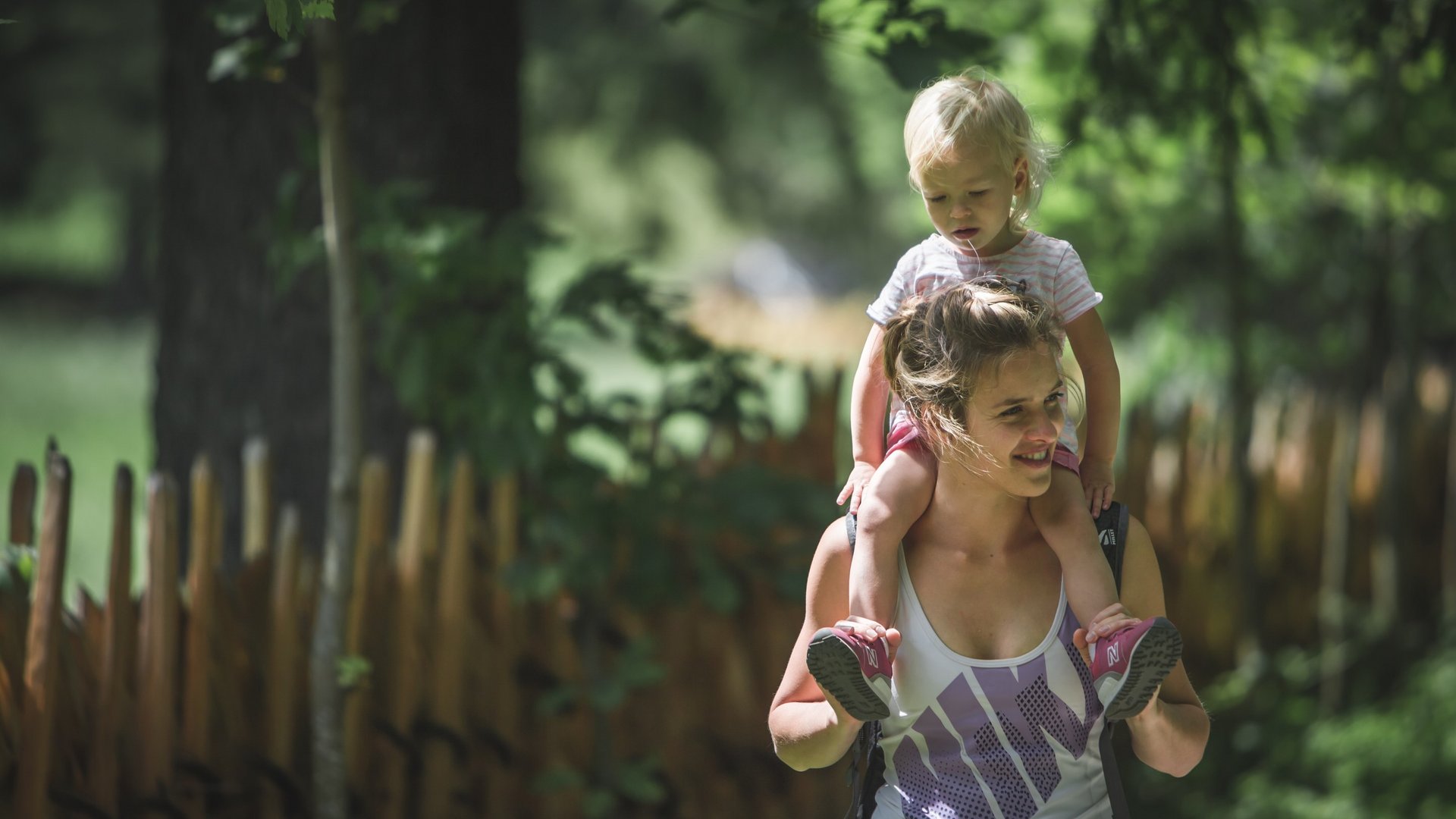 Hotel a Ladurns per famiglie Donna porta un bambino sulle spalle in un bosco soleggiato