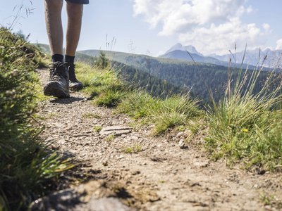 Gudrun Gossensass: Wandern, Radfahren und vieles mehr Wanderer mit Wanderschuhen auf einem Bergpfad mit Landschaft im Hintergrund