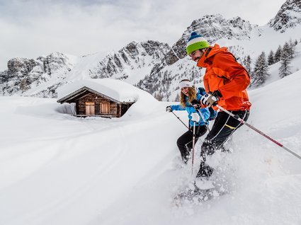 Gudrun in Gossensass: hotel with heart Two people skiing near a snow-covered cabin and mountain backdrop