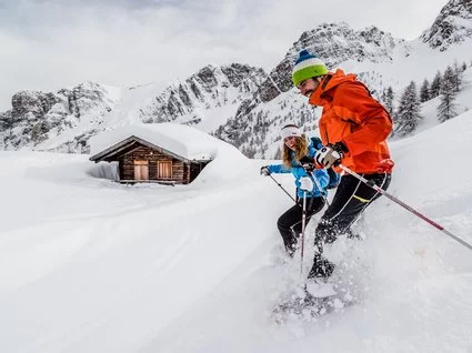 Home Due persone che sciano davanti a baita innevata e montagne