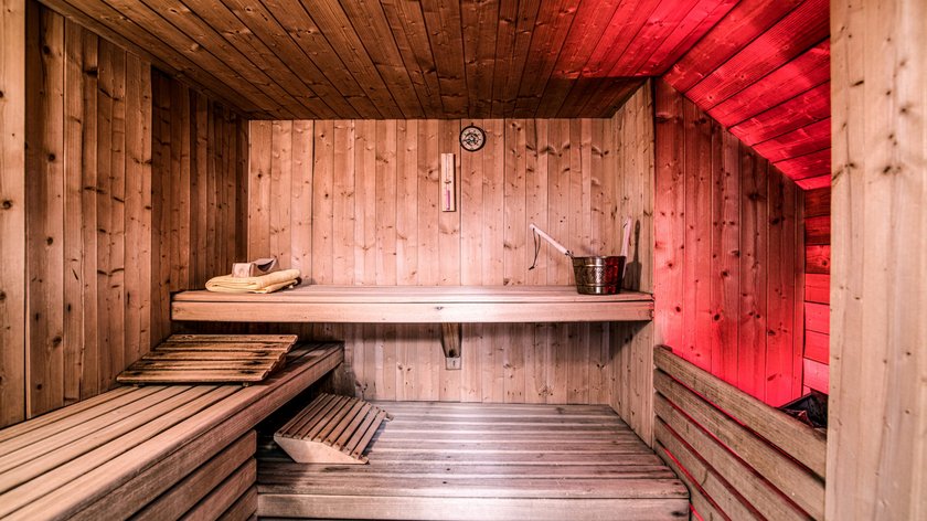 Wellness, Wärme, Wohlbefinden Holzsauna mit roter Beleuchtung, Aufgusskübel und Handtüchern