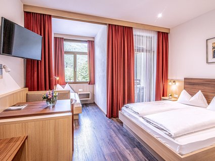 Home Camera d'albergo moderna con letto matrimoniale, divano, tende rosse e TV