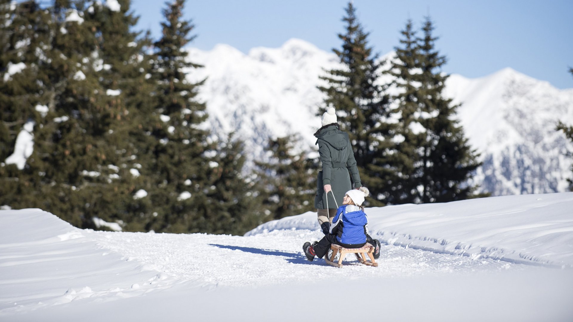 The Ladurns ski area and other winter highlights Woman pulls child on sled through snowy winter landscape with pine trees