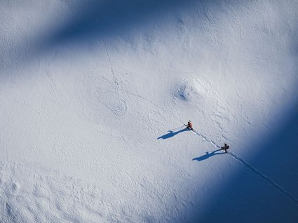 Home Due escursionisti con bastoni camminano su neve con ombre allungate