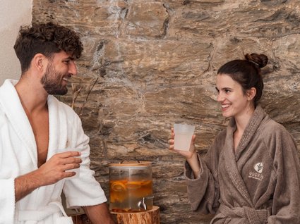 Rilassarsi da Gudrun Uomo e donna con accappatoi bevono acqua davanti a muro di pietra