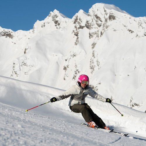Das Skigebiet Ladurns und andere Winter-Highlights Skifahrer mit pinkem Helm auf verschneiter Piste vor Bergpanorama