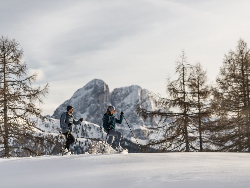 Gudrun in Gossensass: hotel with heart Two people snowshoe hiking in snowy mountain forest with mountain backdrop