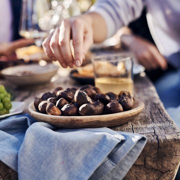 Gudruns Blog: alles über Sterzing, übers Wandern, über Tirol Hand greift geröstete Esskastanien von einem Holztablett auf rustikalem Tisch