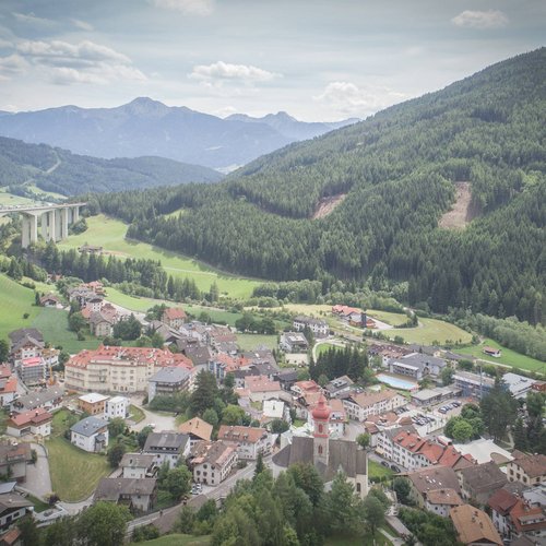 Hotel a Colle Isarco: benvenuti da Gudrun! Veduta aerea di un villaggio in una valle verde con montagne e ponte autostradale