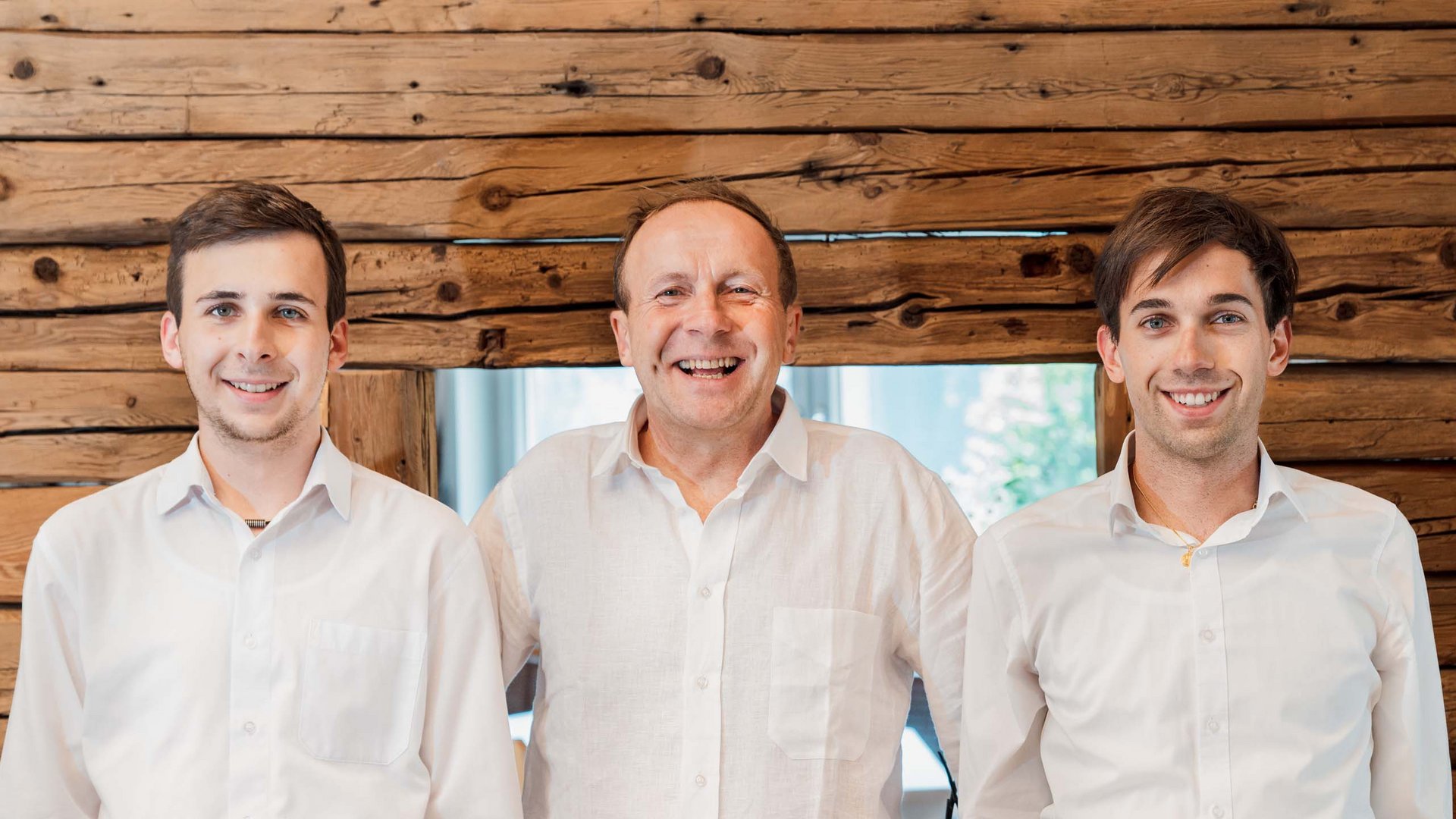 Gudrun in Gossensass: Hotel mit Herz Drei lächelnde Männer in weißen Hemden vor Holzwand