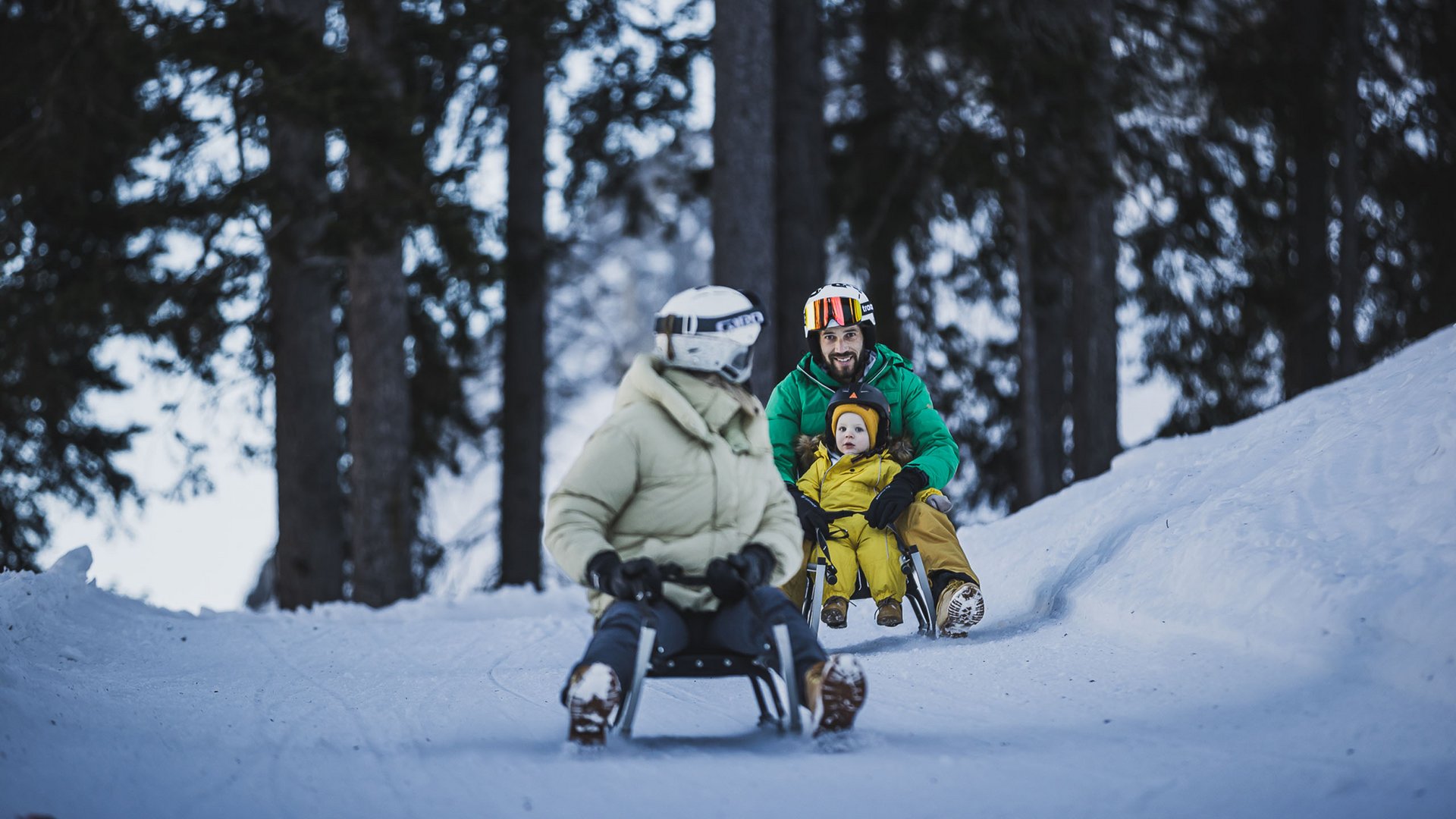 People sledding in snow in winter forest with child