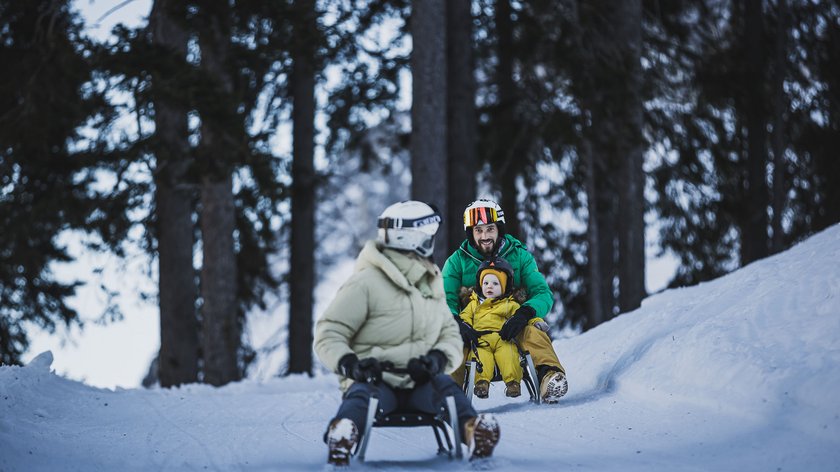 Divertimento sul Monte Cavallo Persone che slittano nella neve in un paesaggio boschivo invernale con bambino