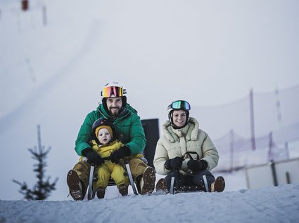 Gudrun in Gossensass: hotel with heart Father with child and woman sledding together on snow downhill
