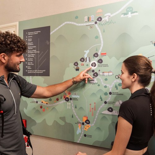 Hotel a Colle Isarco: benvenuti da Gudrun! Uomo indica una mappa murale con sentieri e città a una donna