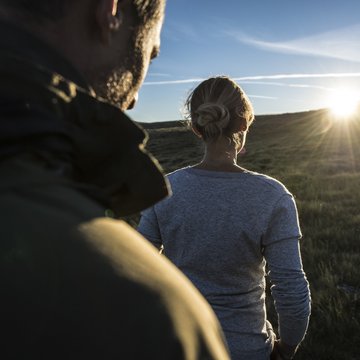 Download-Bereich Frau und Mann wandern bei Sonnenuntergang auf einer grünen Wiese