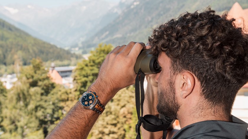 Who is Gudrun? Uomo con orologio guarda attraverso un binocolo verso le montagne