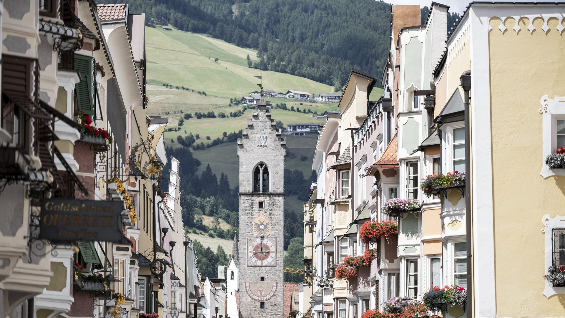 Hotel between Brenner and Sterzing: events Colorful houses with flowers on street facing clock tower and mountains