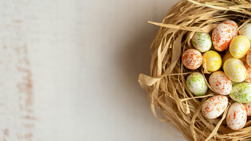 Tradizioni, sapori e costumi Uova di Pasqua colorate in un nido di paglia su sfondo chiaro
