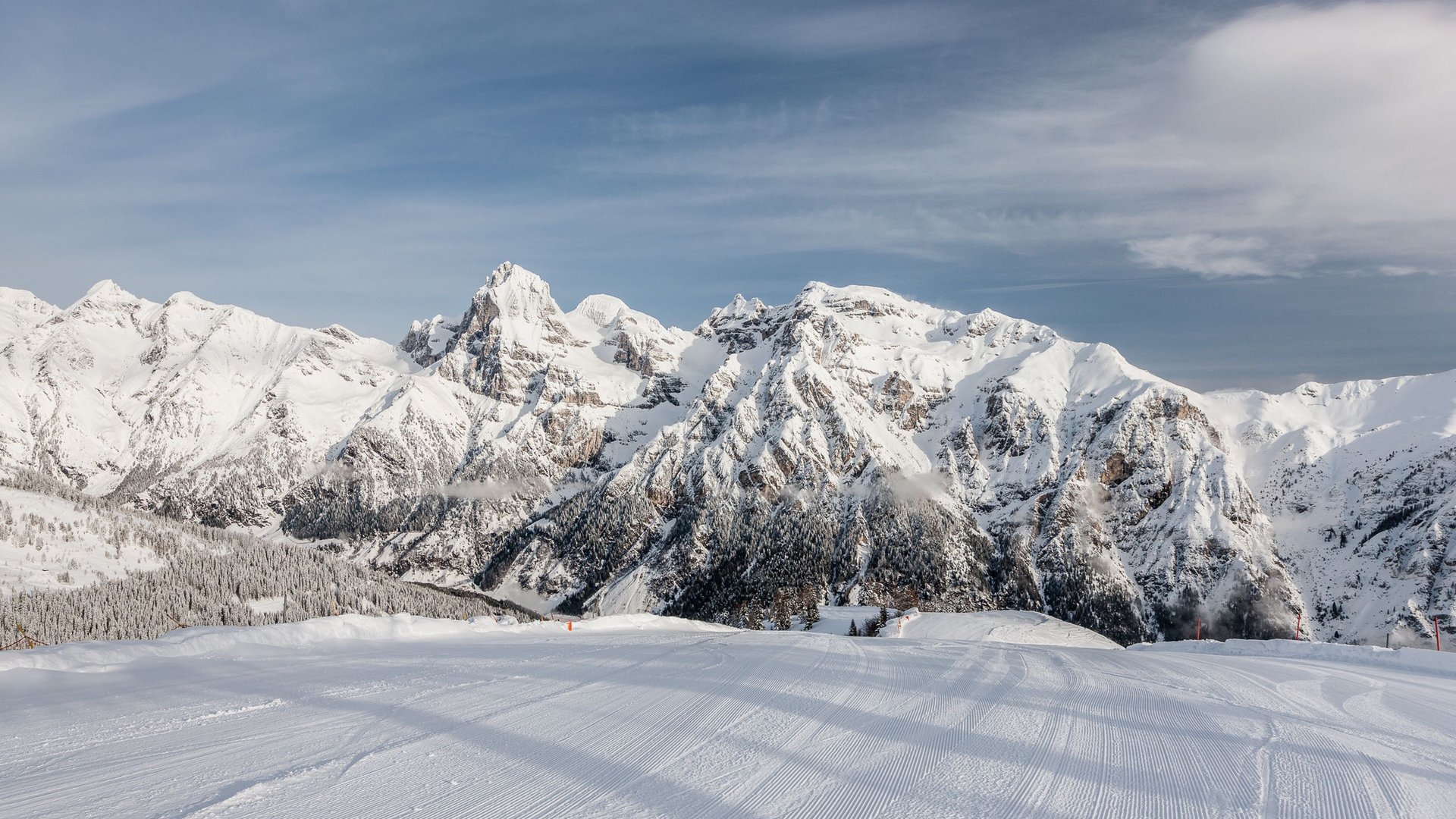 Freshly groomed ski slope with snowy mountains under blue sky