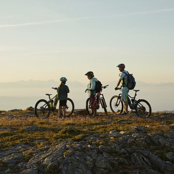 Gudruns Blog: alles über Sterzing, übers Wandern, über Tirol Drei Radfahrer mit Helmen stehen auf felsigem Gipfel bei Sonnenuntergang