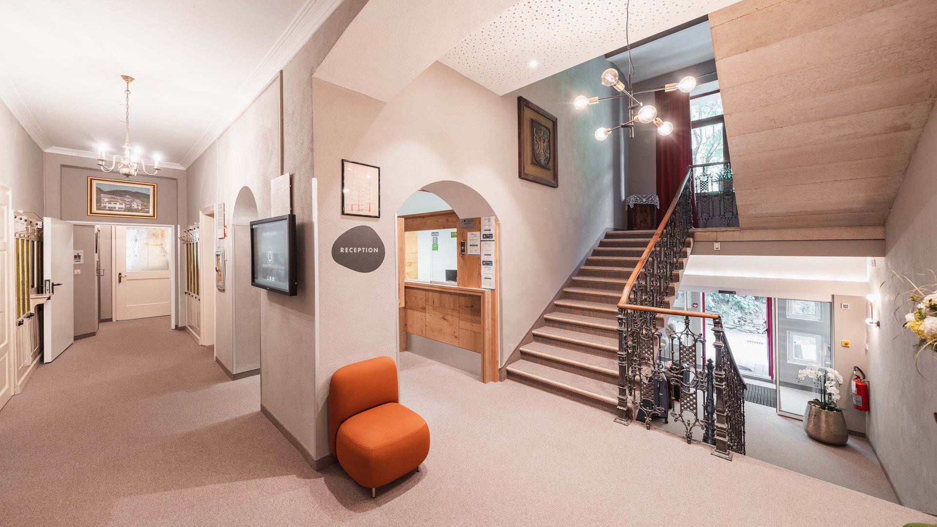 Hotel a Colle Isarco: benvenuti da Gudrun! Ingresso luminoso dell'hotel con reception, scale e poltrona arancione