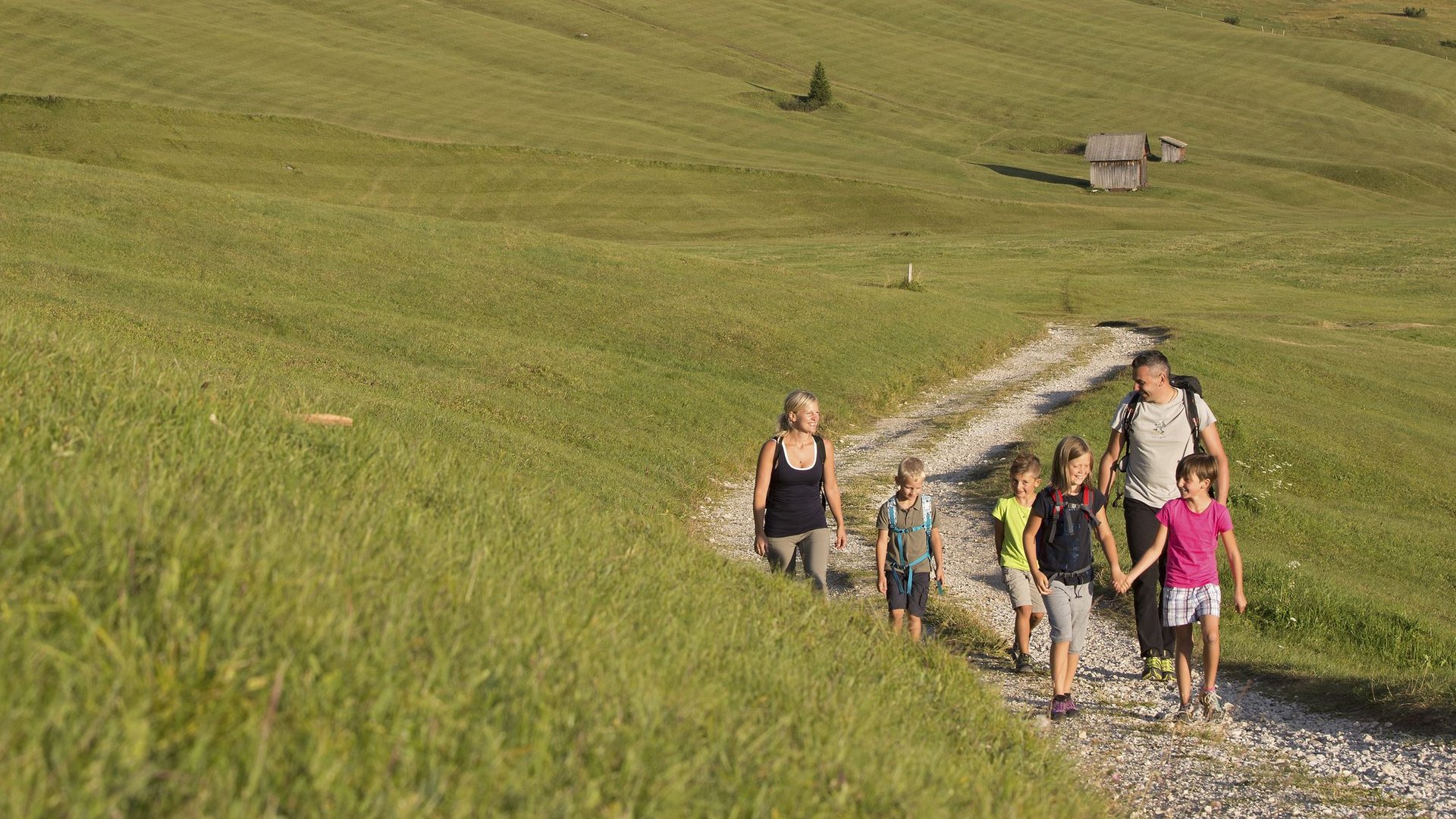 Hotel a Ladurns per famiglie Famiglia che cammina su un sentiero verde nelle Alpi con montagne sullo sfondo