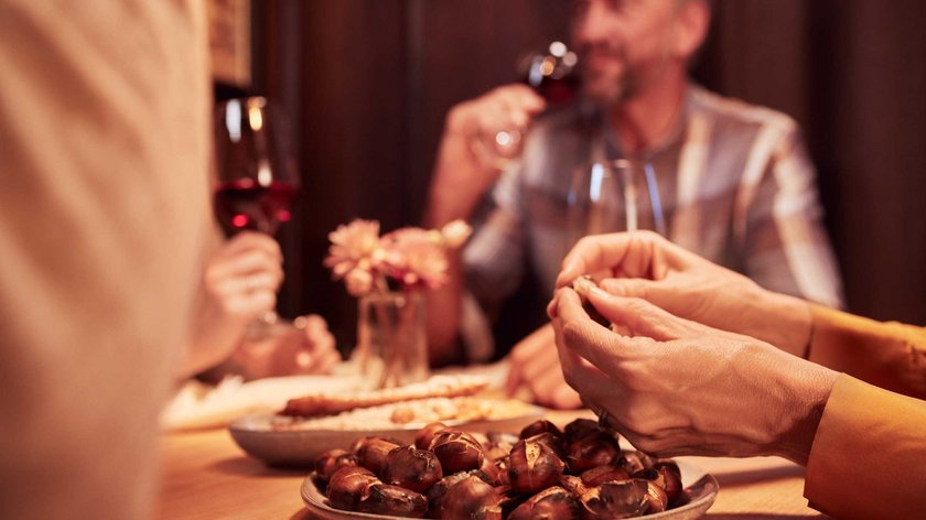 Gudrun stellt vor: Törggelen – traditionelle Genusstage im Herbst Menschen essen geröstete Kastanien und trinken Rotwein in geselliger Runde