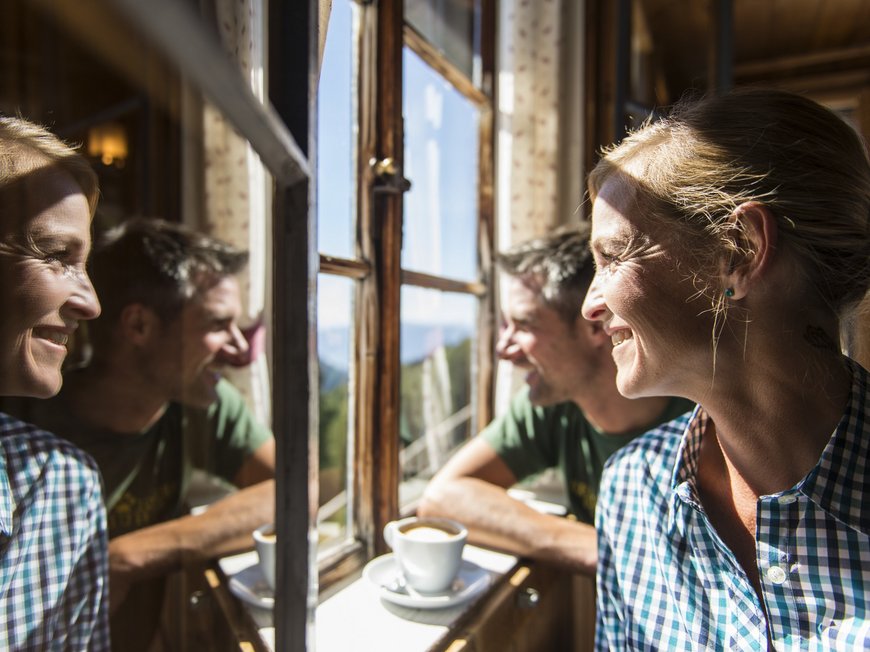 Schwimmbad in Sterzing und mehr – das gibt’s hier alles. Frau und Mann lächeln an einem sonnigen Fenster mit Kaffee