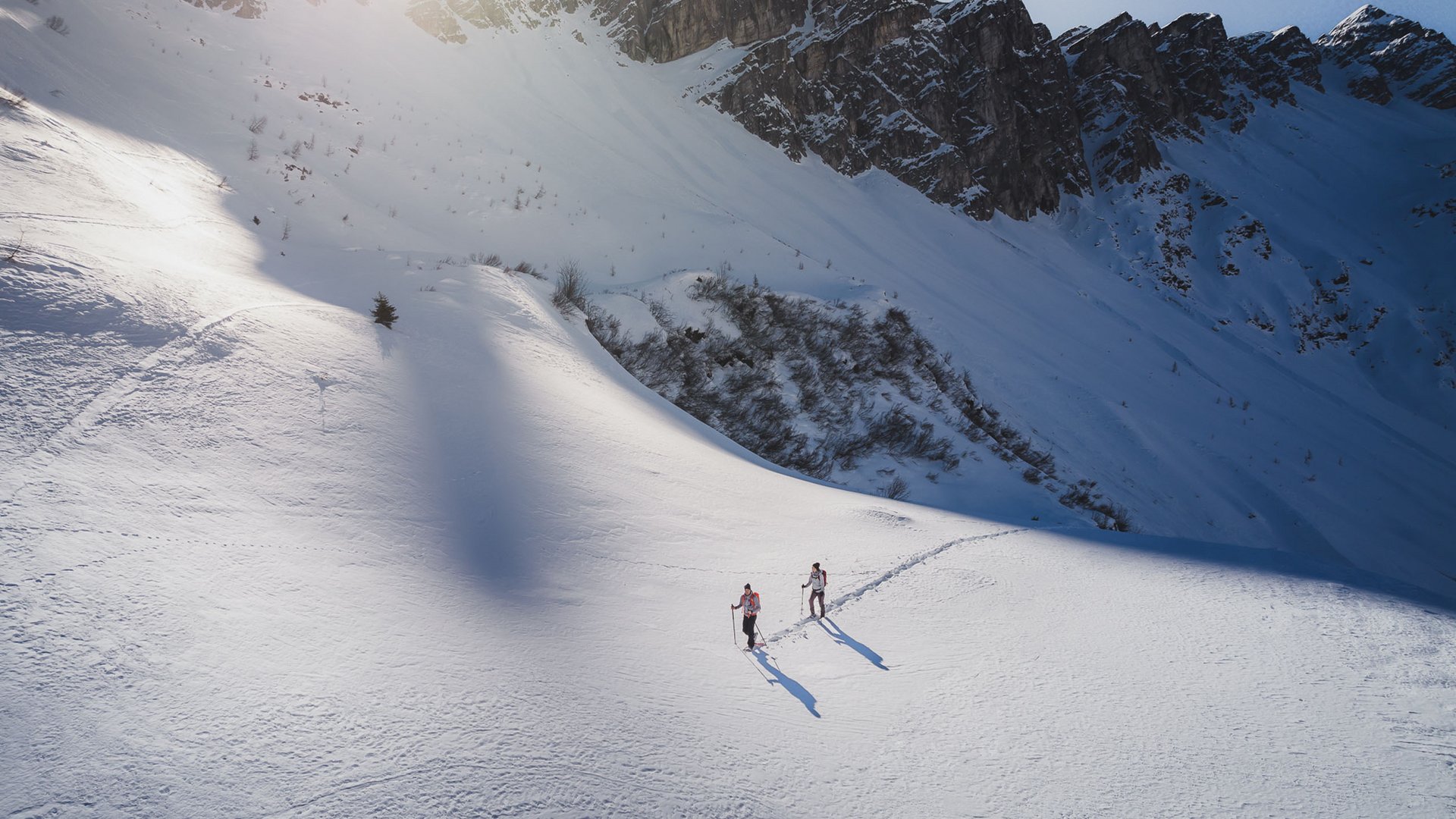 Gudrun Gossensass: Wandern, Radfahren und vieles mehr Zwei Wanderer im Schnee vor felsigen Bergen bei Sonnenlicht