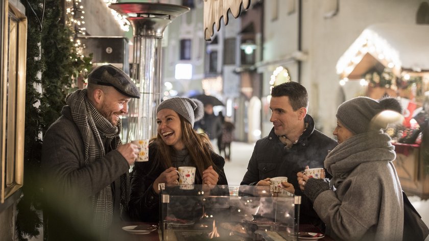 Magia natalizia nella Valle Isarco: i migliori mercatini di Natale Quattro persone bevono bevande calde a un tavolo riscaldato all'aperto in inverno