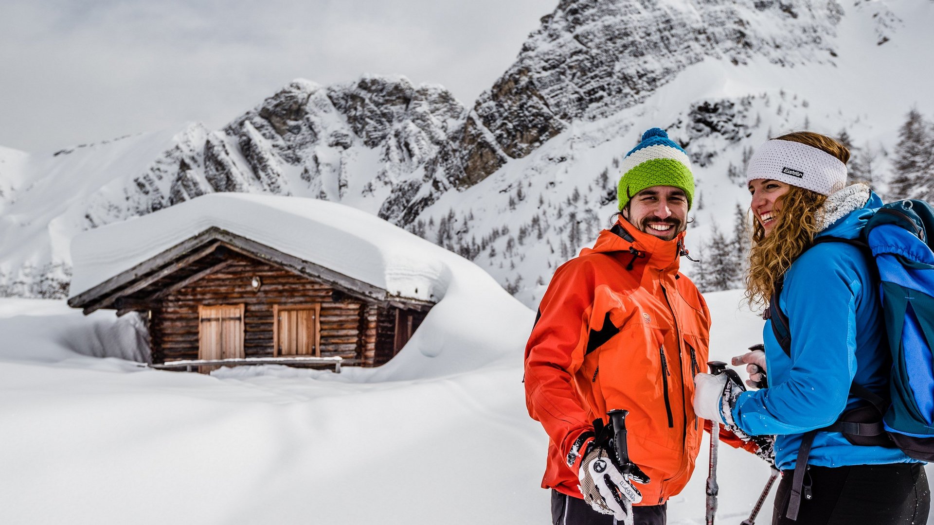 Das Skigebiet Ladurns und andere Winter-Highlights Zwei Skifahrer mit Stöcken vor verschneiter Hütte in den Bergen
