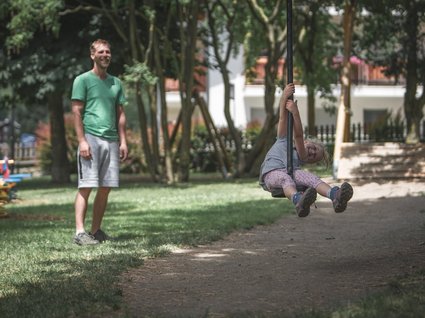 Gudrun in Gossensass: Hotel mit Herz Mädchen schwingt auf Spielplatzseil, Mann beobachtet lächelnd im Hintergrund