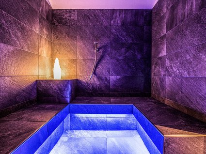 Home Stanza benessere moderna con vasca illuminata di blu e viola e pareti di pietra