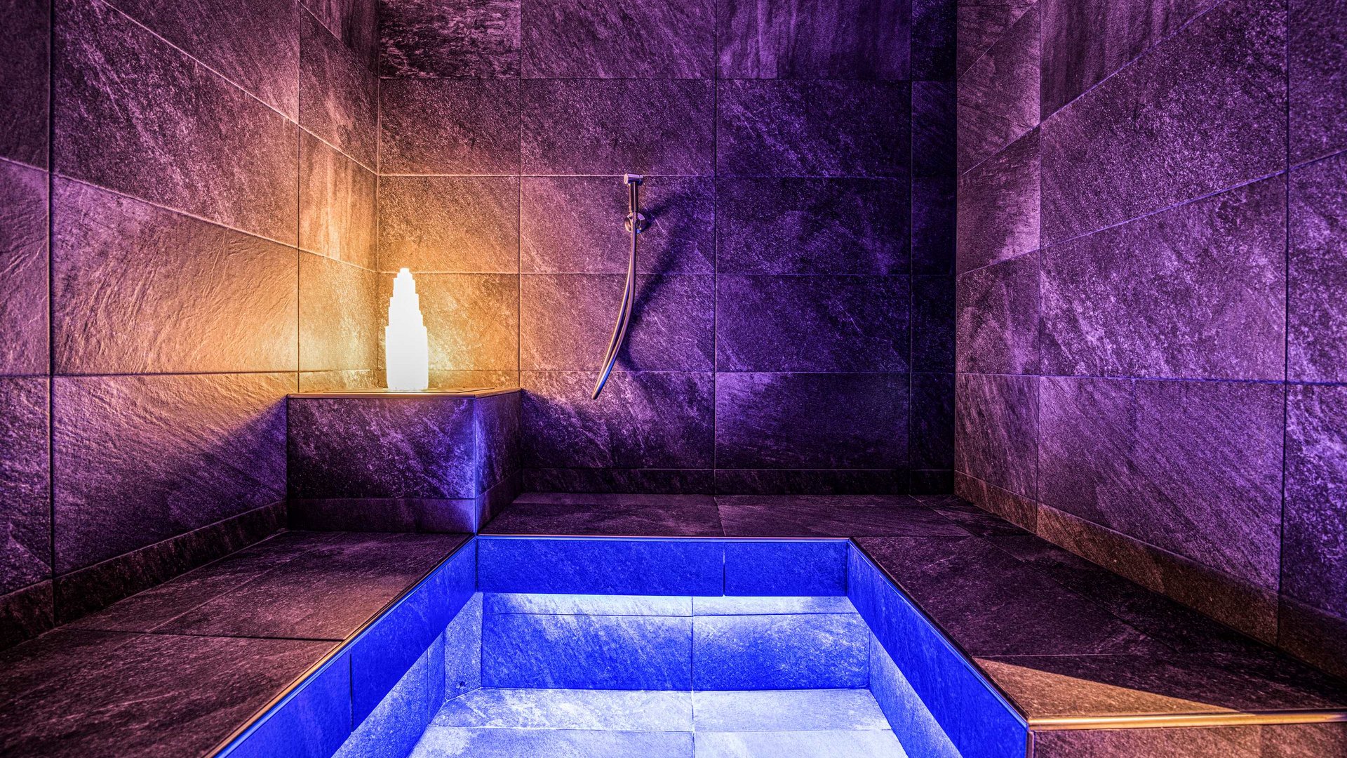 Explorer and wellness hotel near Sterzing Modern wellness room with blue and purple lit pool and stone walls