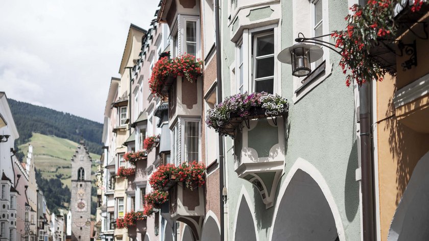 Shopping im Urlaub Bunte Häuser mit Blumen in Balkonen und Bogen auf einer Straße mit Bergkulisse