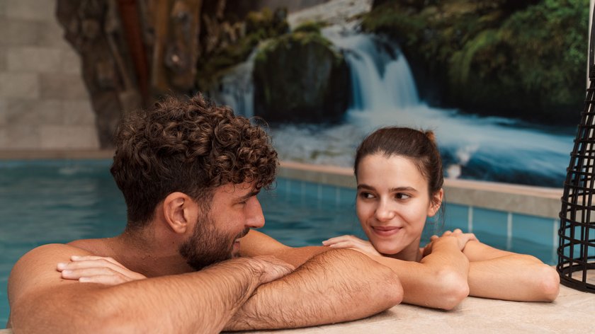 Abkühlung gefällig? Paar entspannt im Pool mit Wasserfallbild im Hintergrund