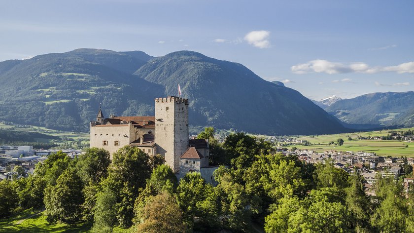 Die Messner Mountain Museen Burg auf bewachsenem Hügel vor Berglandschaft und Dorf