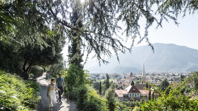 Ein Ausflug nach Bozen Paar spaziert auf einem Pfad mit Blick auf eine Stadt und Berge im Hintergrund