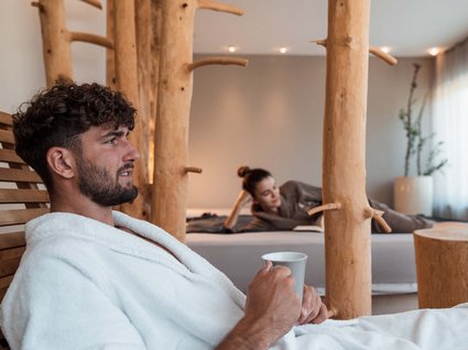 Explorer and wellness hotel near Sterzing Man in white robe holding cup, woman relaxing in the background