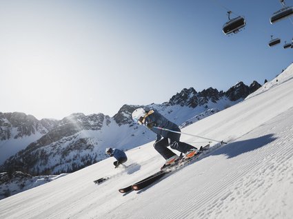 Gudrun in Gossensass: hotel with heart Two skiers on groomed slope under clear blue sky in the mountains