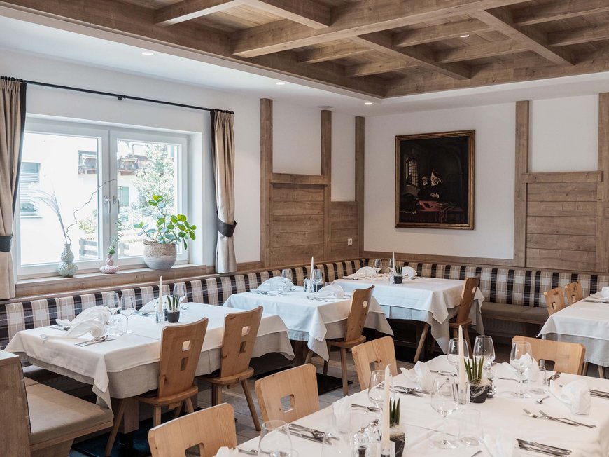 Hotel a Colle Isarco: benvenuti da Gudrun! Sala da pranzo elegante con soffitto a travi in legno e tavoli apparecchiati con tovaglie bianche