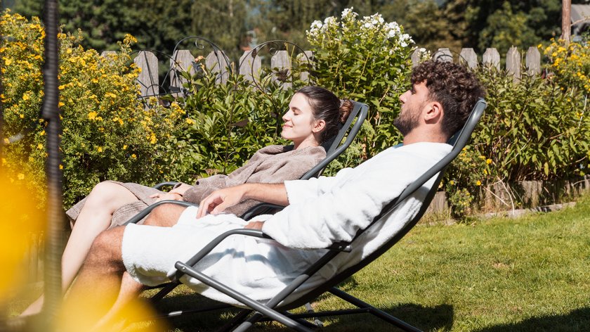 Was uns jetzt verzaubert Paar entspannt sich im Garten in Bademänteln auf Liegestühlen
