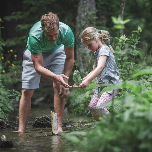 Wandern in Sterzing und Umgebung Mann und Mädchen erforschen einen Bach im Wald gemeinsam