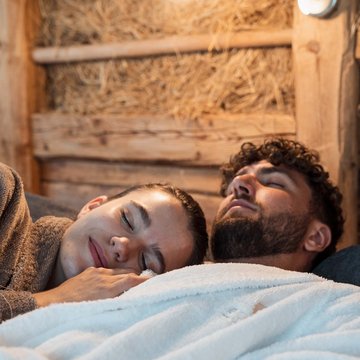Gudrun in Gossensass: Hotel mit Herz Paar in Bademänteln entspannt liegen auf Holzwand Hintergrund