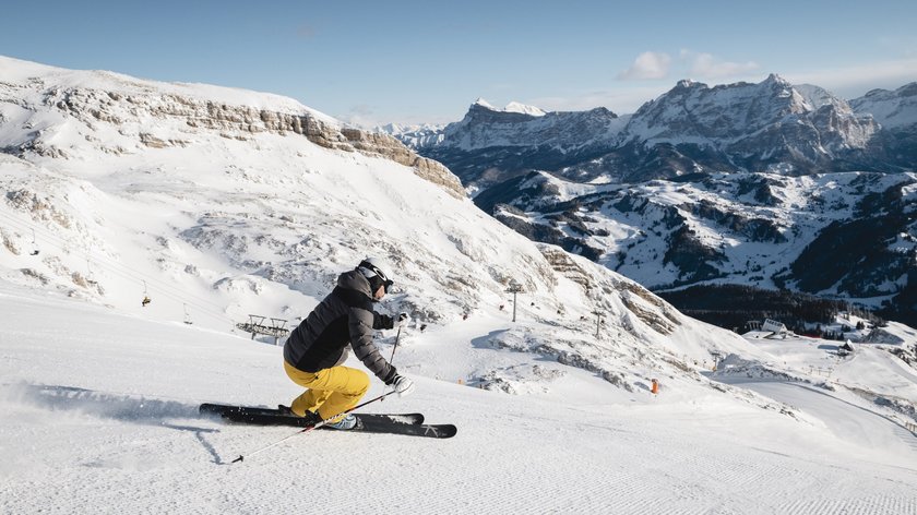 Sellaronda is calling! Sciatore con pantaloni gialli scende su pista innevata con montagne sullo sfondo